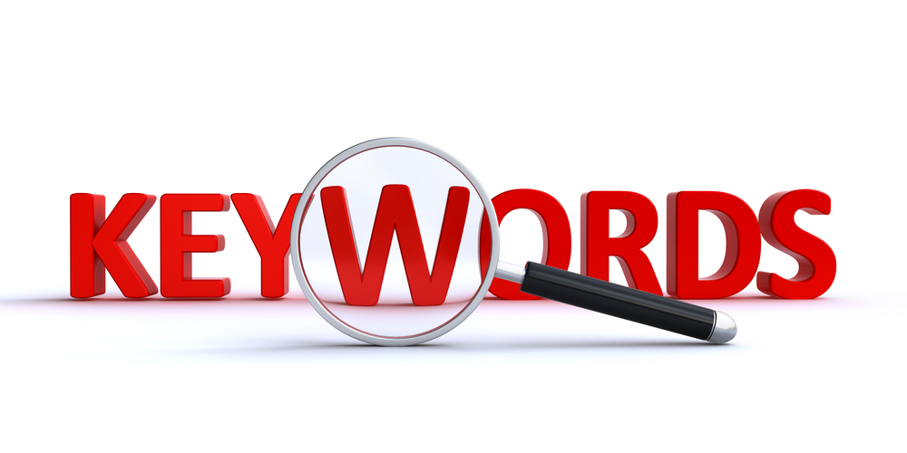 3D red text spelling 'KEYWORDS' with a magnifying glass focusing on the word, symbolizing keyword analysis or research.